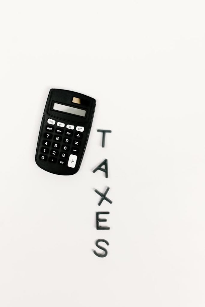 Black calculator and letter tiles spelling TAXES on a smooth white background, symbolizing financial calculations.